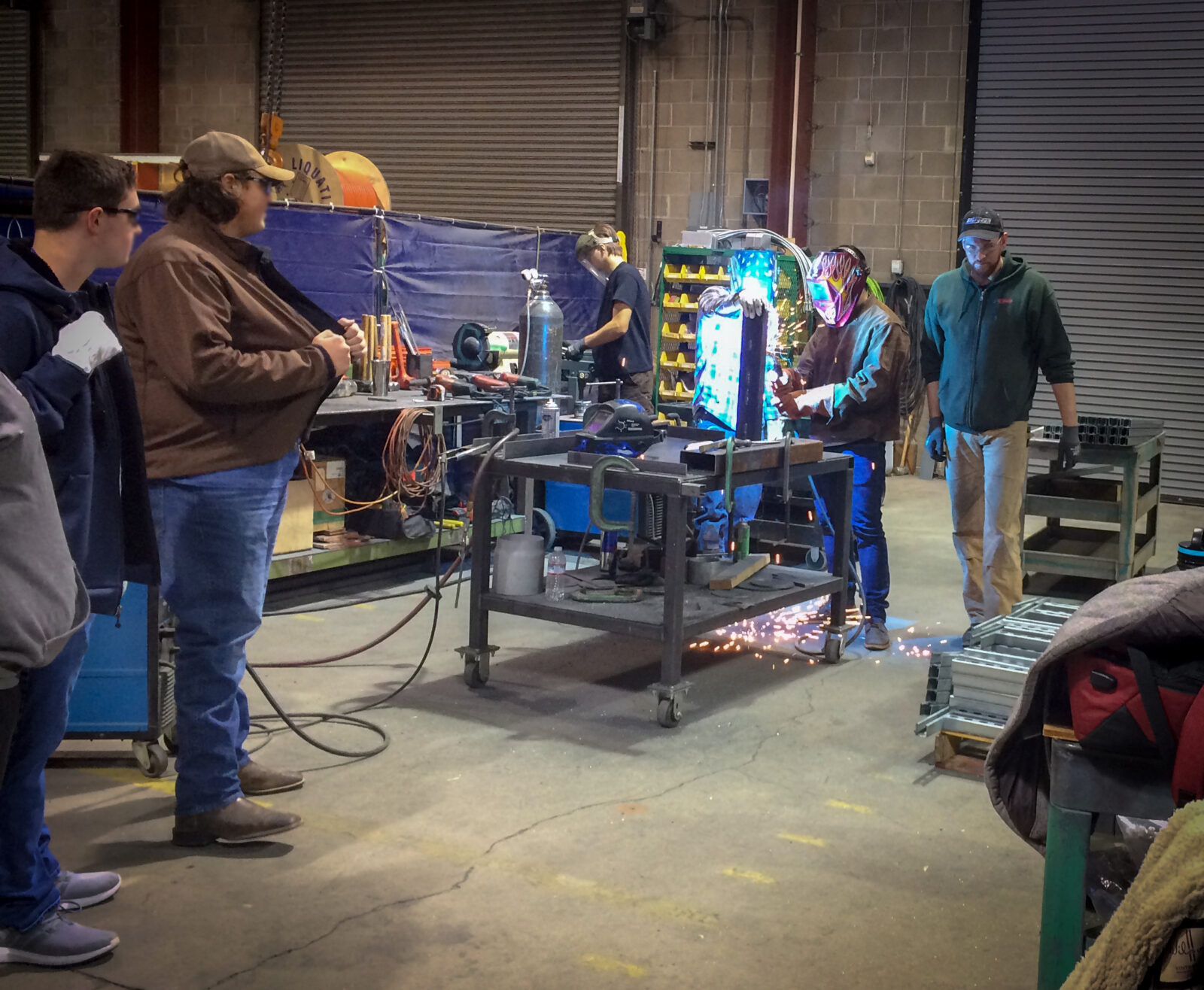 High school students at an electrical trade event. One is welding while others look on.